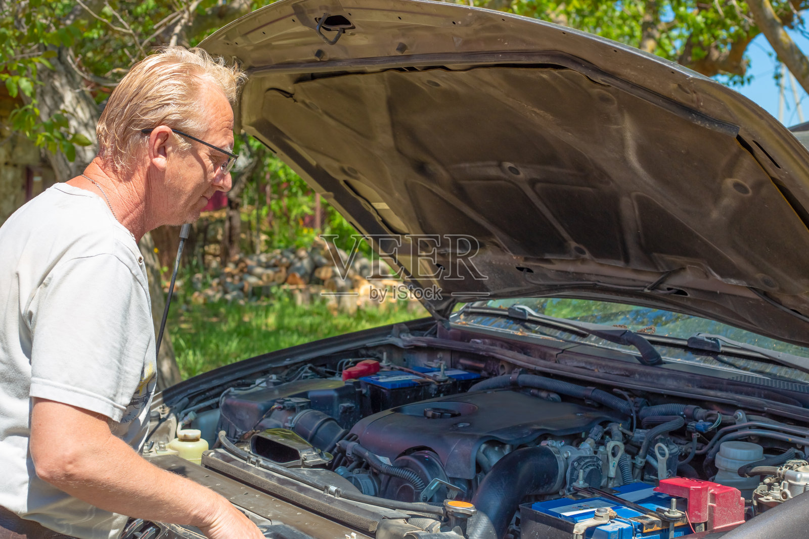 一个金发的成年欧洲老人在看一辆汽车的引擎盖下面，试图处理故障照片摄影图片