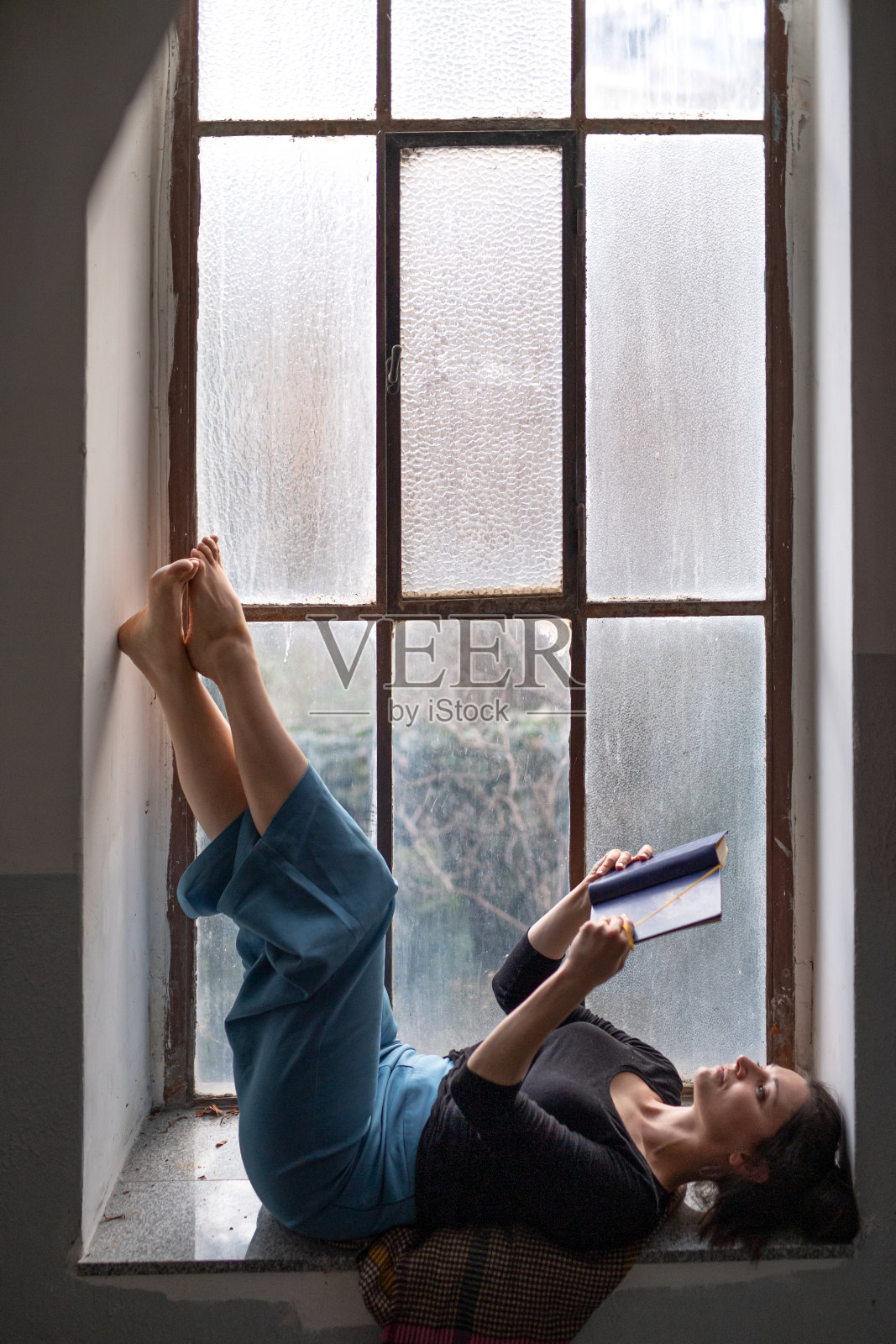 一个女人躺在又旧又脏的窗台上看书。照片摄影图片