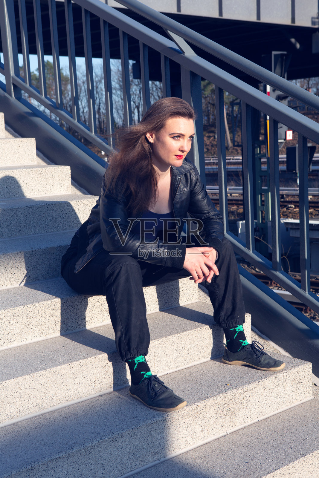 穿着皮夹克坐在户外火车站的楼梯台阶上的年轻女子照片摄影图片