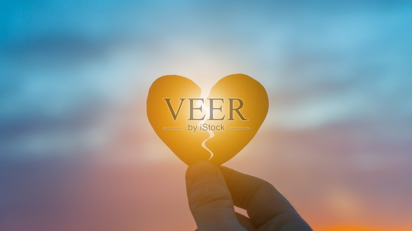 夕阳下，一只手抱着一颗破碎的心。照片摄影图片