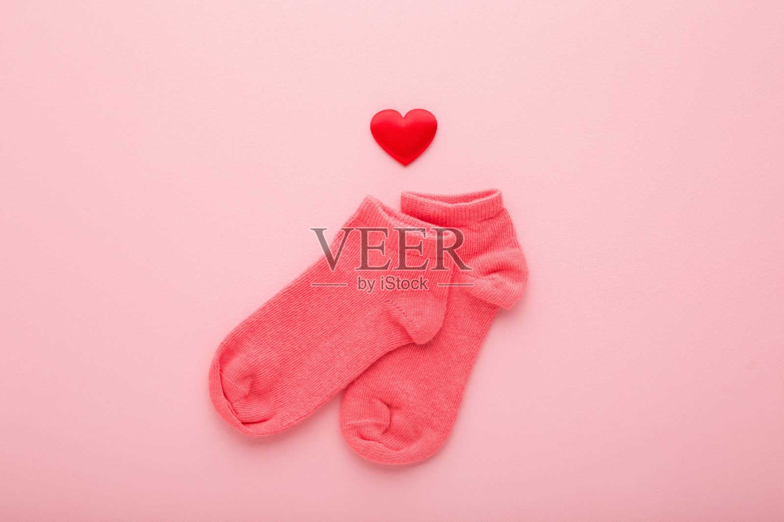 短袜女婴和红色的心型浅粉红色的桌子背景。柔和的颜色。特写镜头。自顶向下的观点。照片摄影图片