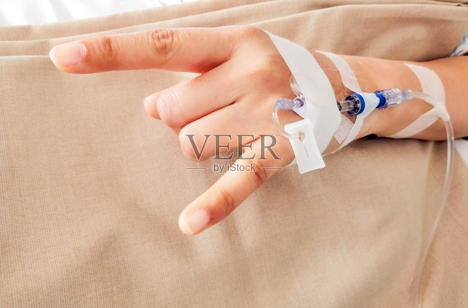 做出“我爱你”手势的病人坐在医院的床上，手上拿着盐溶液线。照片摄影图片