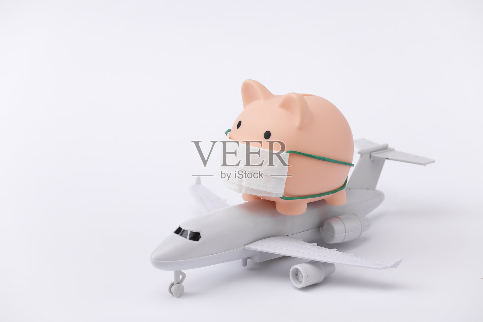 医疗面具里的存钱罐，白色背景上是客机图案。2019冠状病毒病大流行期间的旅行照片摄影图片