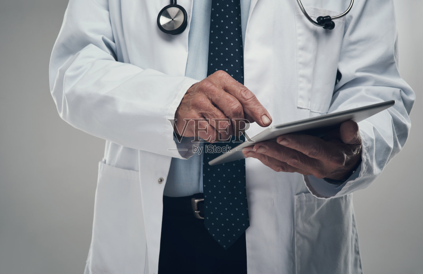 照片中，一名年长的男性医生在工作室里使用数码平板电脑，背景是灰色照片摄影图片