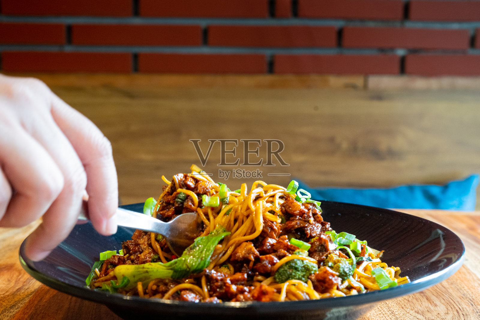 在德里旅行时，一名女子拿着叉子从一个小街边小吃店的木桌上的黑碗里捡起印度支那满族客家街头小吃面条照片摄影图片