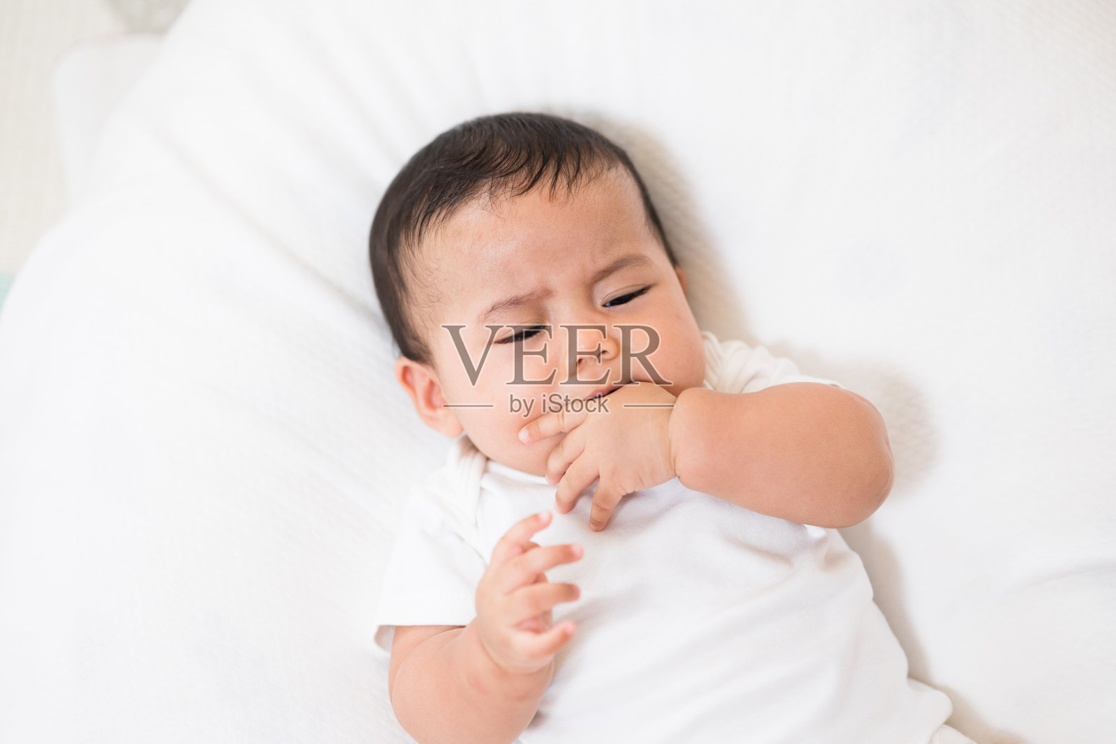 一个穿着白色连衣裙的可爱婴儿在哭。和父母呆在家里照片摄影图片