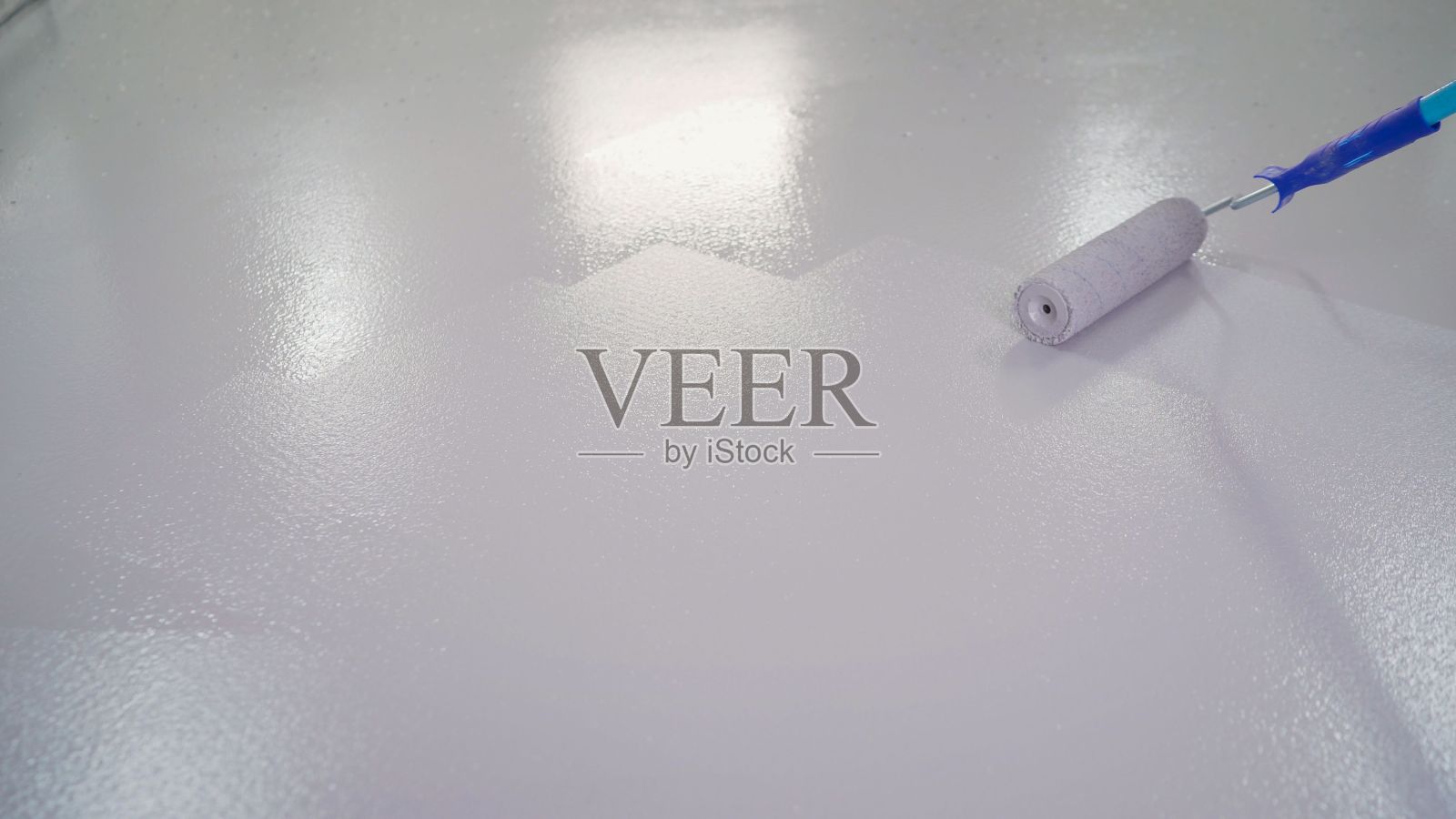 男人在刷地板。地板用滚轴涂成白色。蓝色漆辊，白色背景照片摄影图片