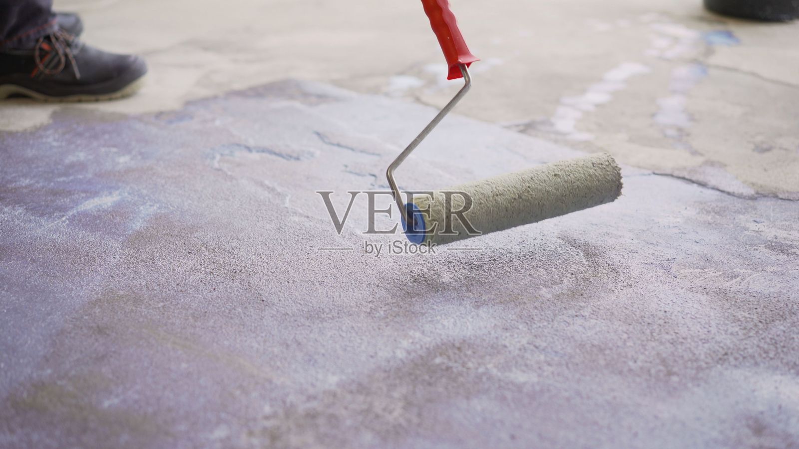 混凝土地板底漆是表面加固的最后准备阶段。用长柄滚轮给混凝土地面打底漆。地板上启动过程。照片摄影图片