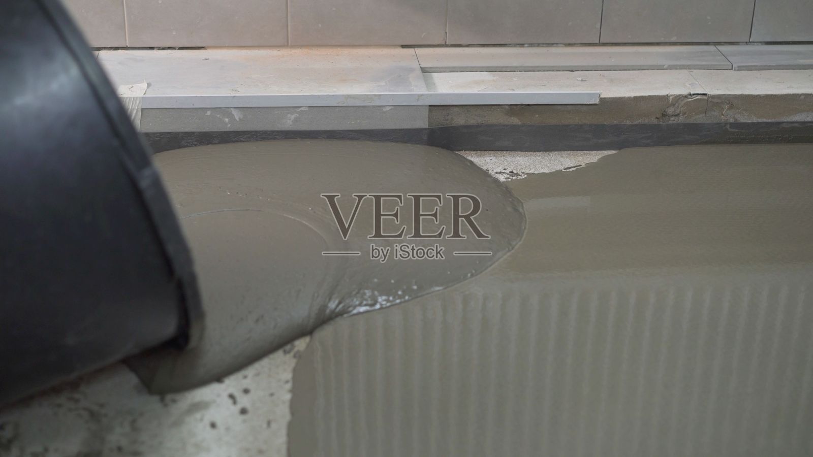 在正在施工的建筑物的地板表面抹平干的水泥-砂混合物。用手工工具填充地板的混凝土工作。用灰浆填地板的过程。照片摄影图片