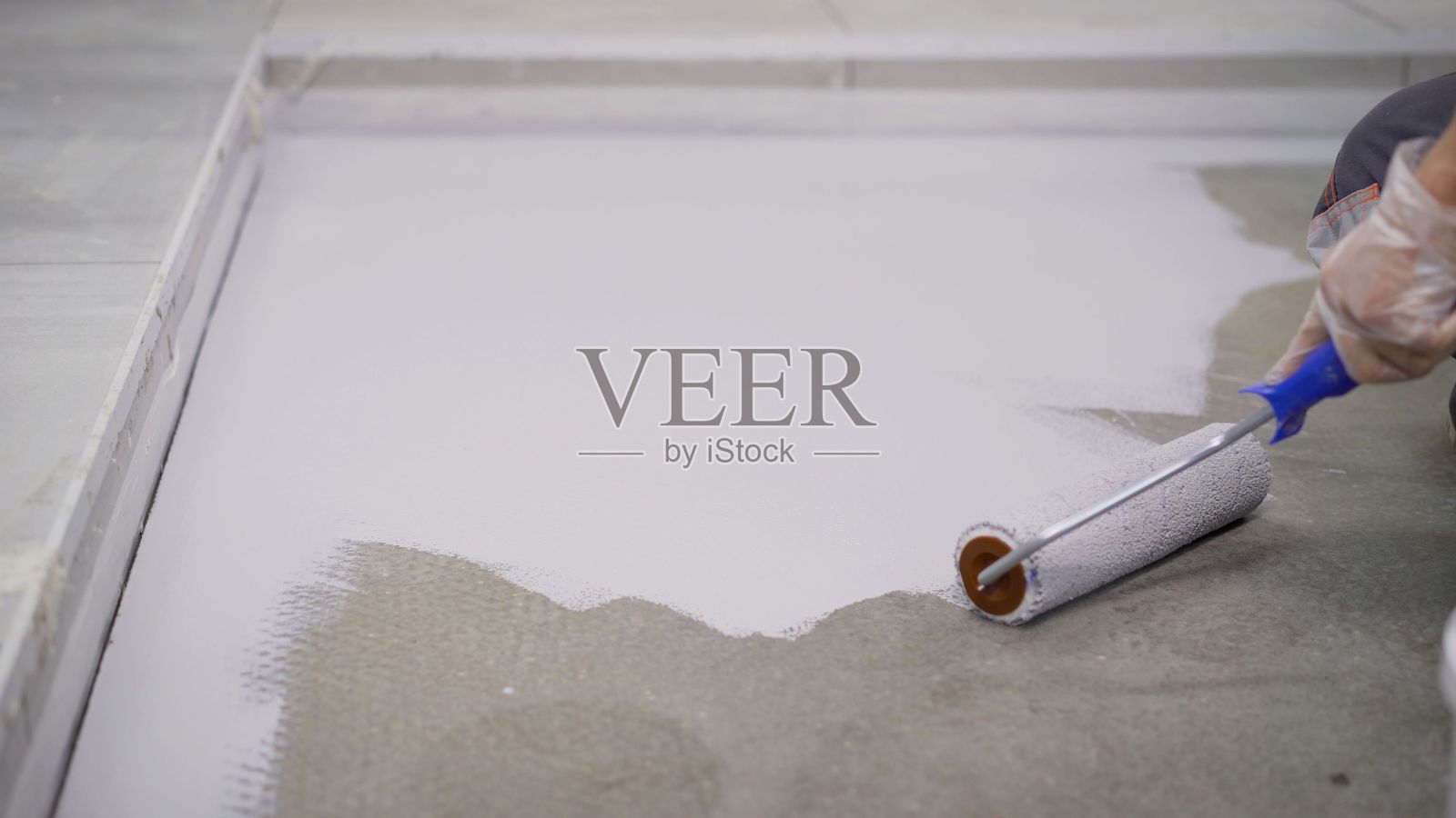 地板上画画。脏乱的修理和改建。一个工人用滚轴把地板涂成白色。混凝土地板是用白漆漆的。背景散焦的油漆滚轴。照片摄影图片