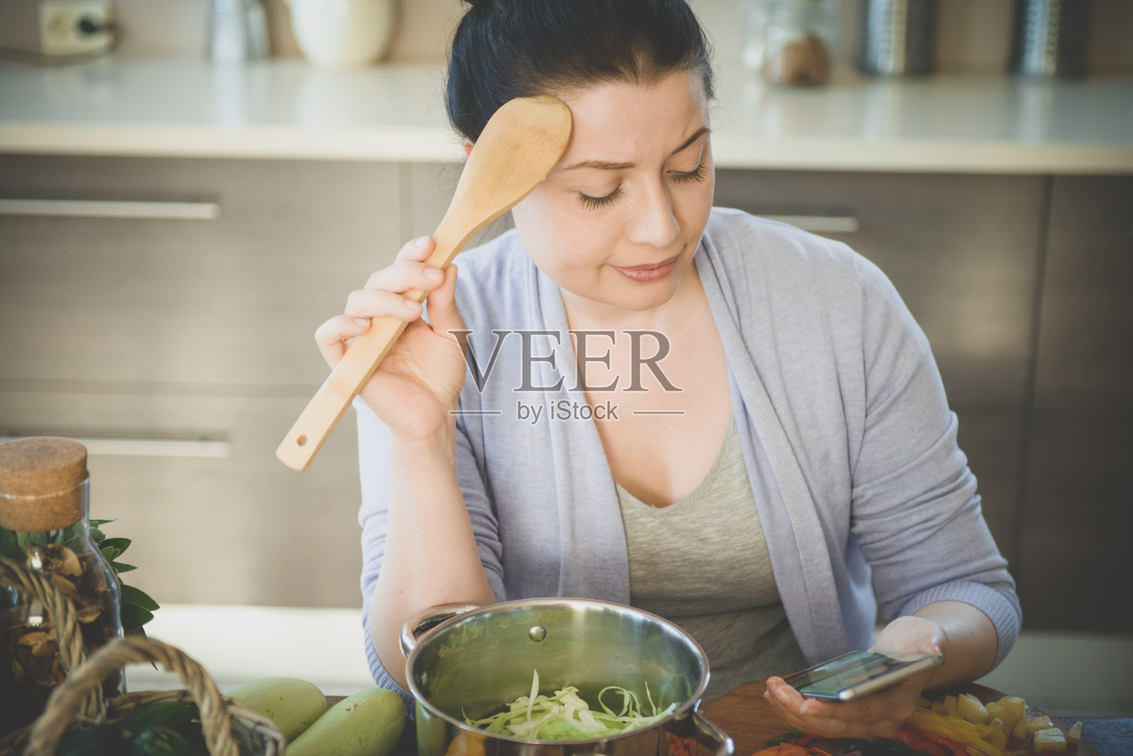 在厨房里做饭的女人(带着智能手机)照片摄影图片