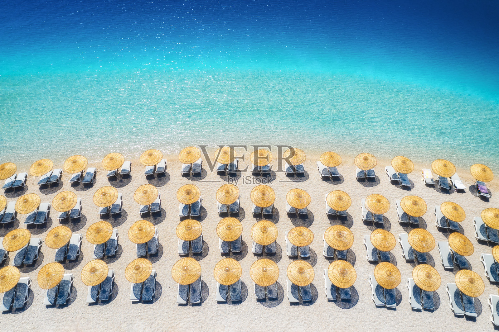 海面鸟瞰图，空旷的沙滩与日光浴床和雨伞在夏天的晴天。土耳其Oludeniz的蓝色泻湖。热带景观与清澈的绿松石水，躺椅。旅游和休闲照片摄影图片