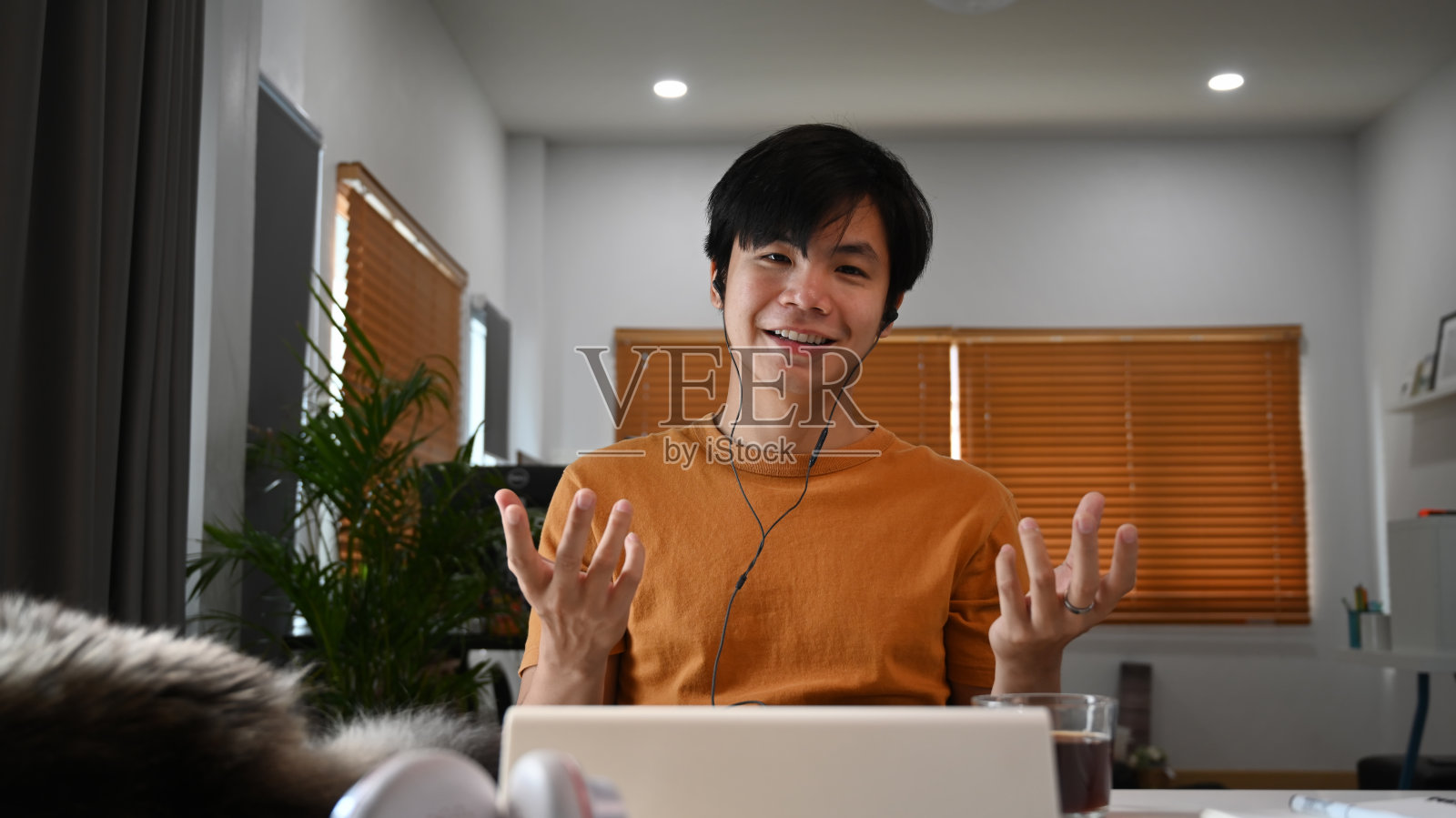 正面的年轻亚洲男子戴着耳机和同事视频通话。照片摄影图片