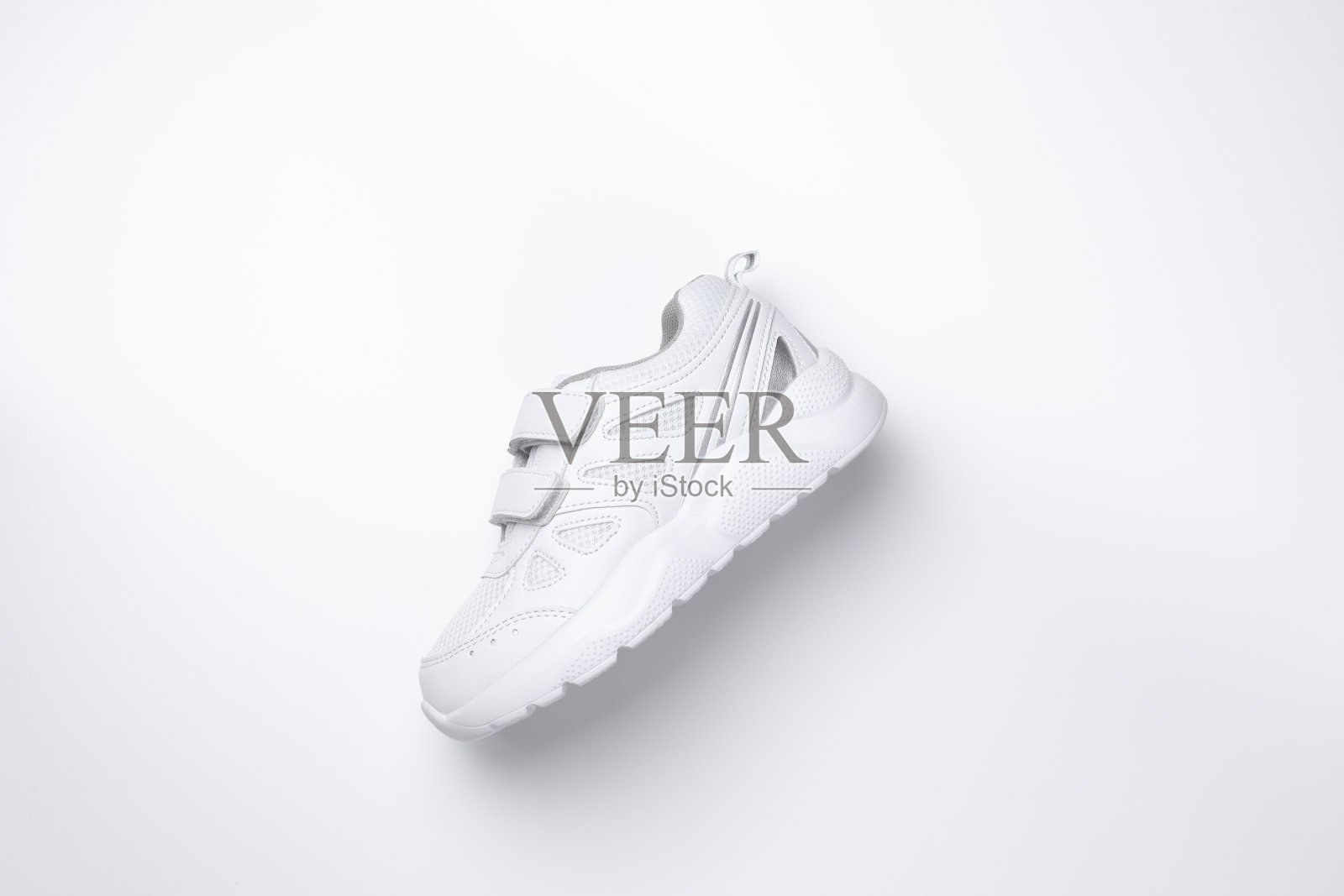 平放一只白色小球鞋，用维可牢尼龙搭扣固定在侧面，中间有柔和的阴影，孤立在白色背景上照片摄影图片
