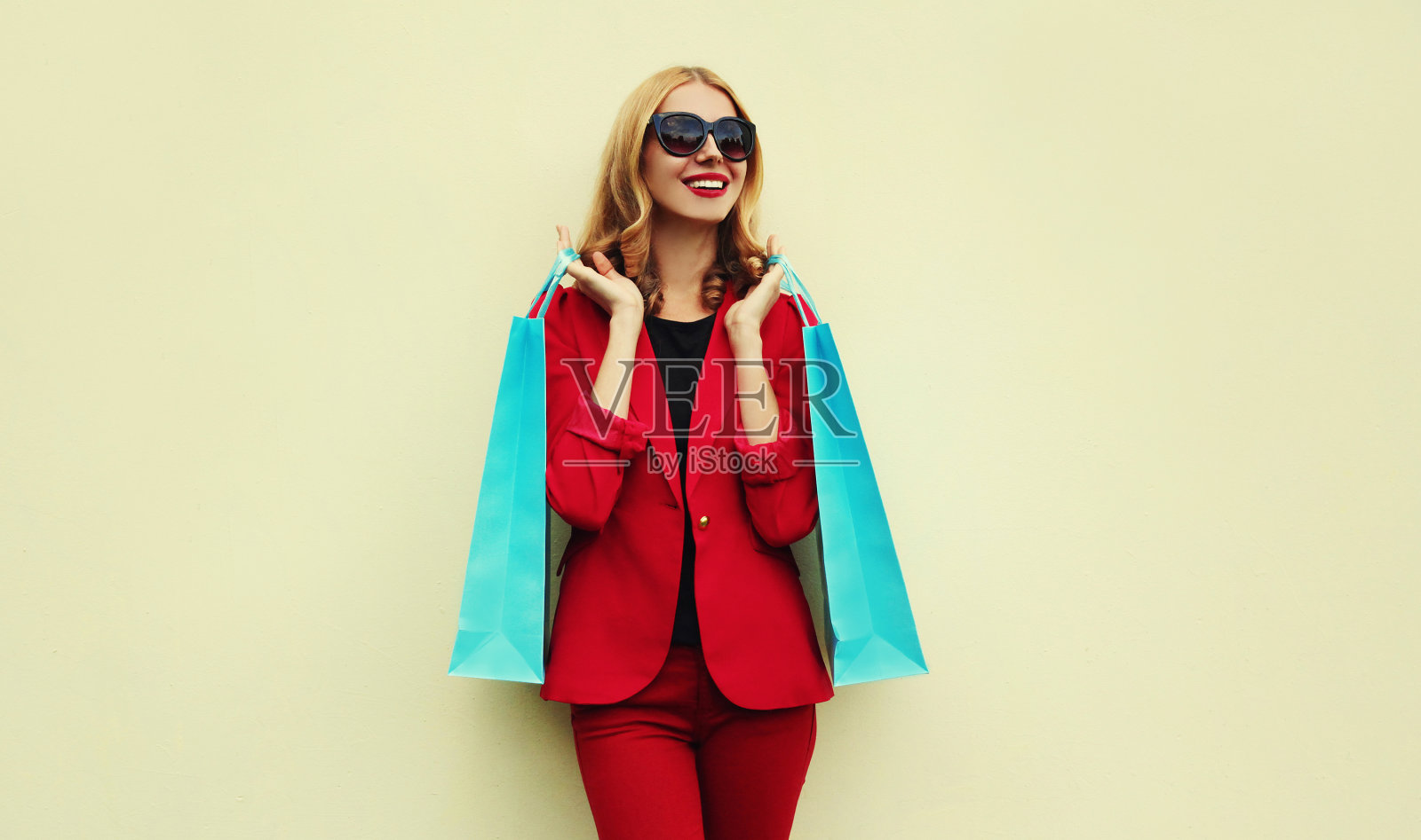 一个快乐微笑的年轻女子的肖像与购物袋穿着一件红色的商务外套的背景照片摄影图片