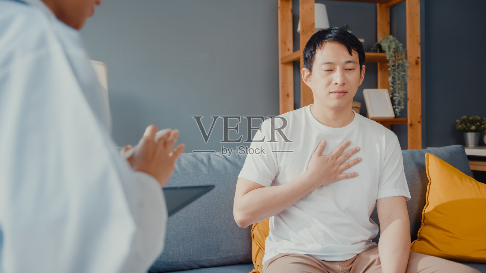 年轻的亚洲女性专业医生医生使用数字平板电脑分享良好的健康测试消息与快乐的男性病人坐在沙发上。照片摄影图片