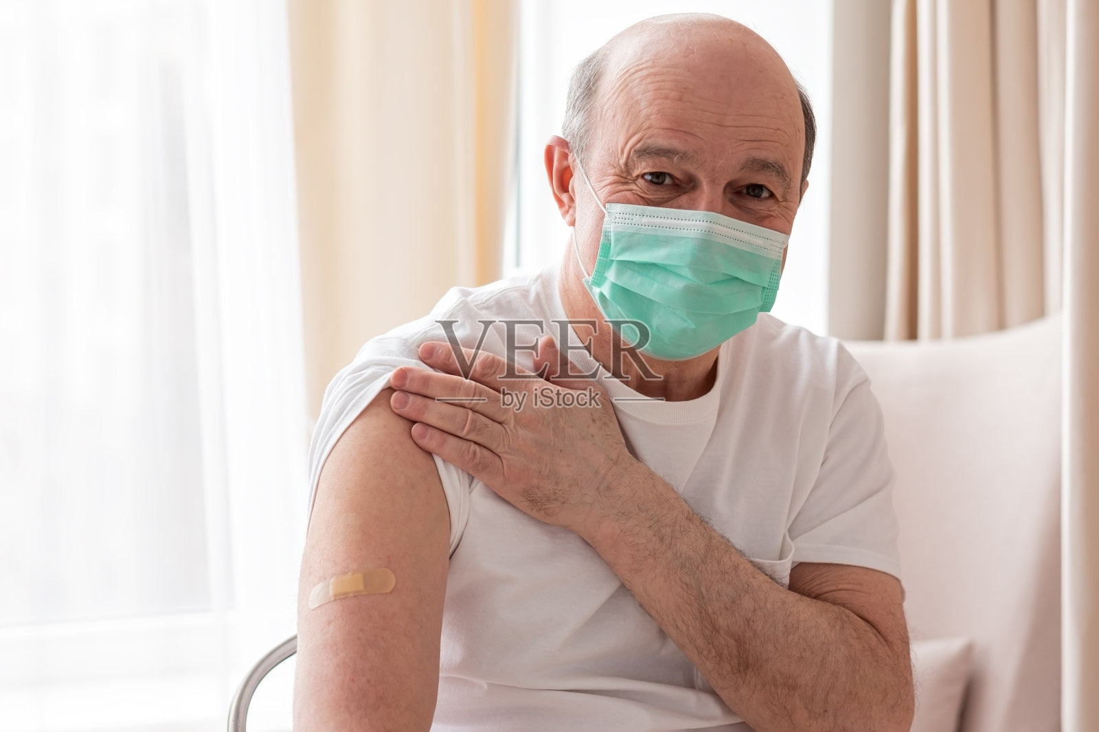 年长的西班牙男子戴着口罩，显示接种疫苗的手臂。照片摄影图片