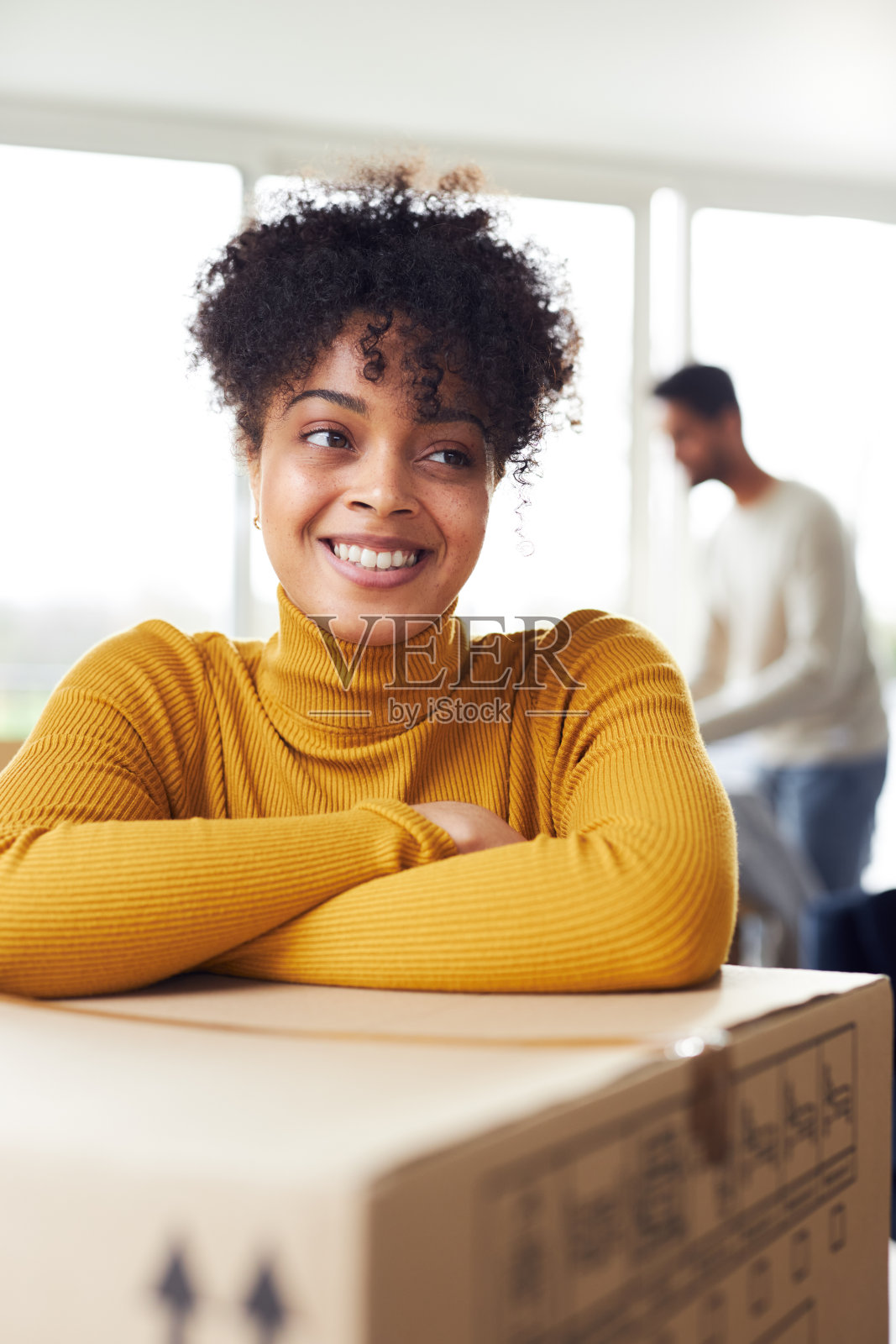 搬家当天，在新家休息室里的快乐夫妇的肖像，女人靠在搬家箱上照片摄影图片