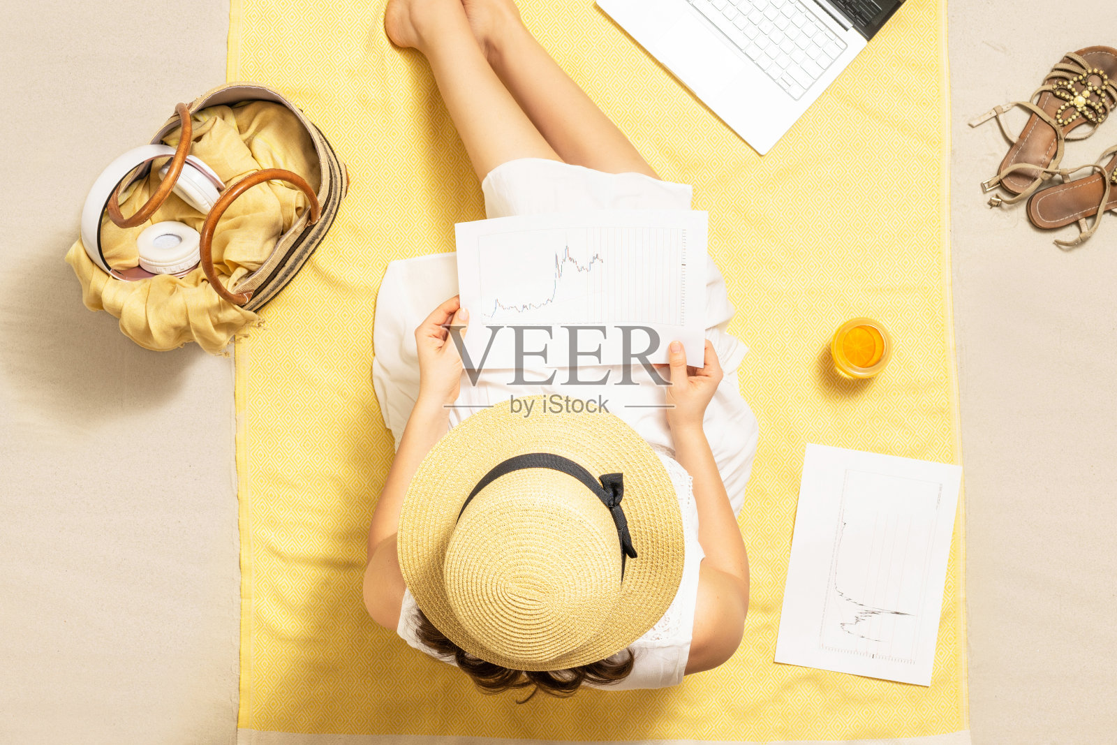 女商人自由职业者坐在沙滩浴巾上喝着果汁，用笔记本电脑处理图形和图表。暑假。鸟瞰图照片摄影图片