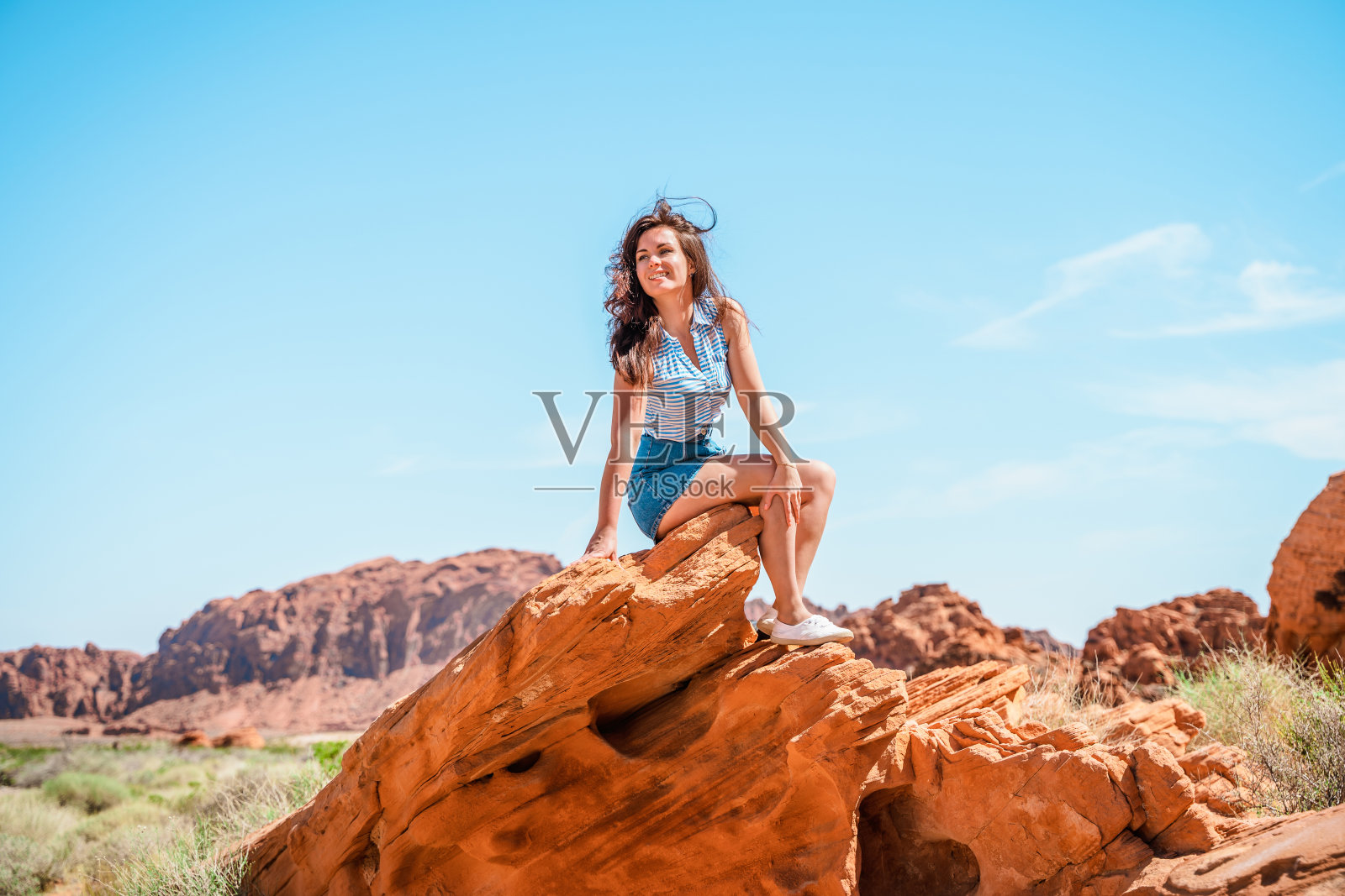 一个年轻的女人正在欣赏内华达火谷的景色，看到红色的岩石在沙漠景观中切割成带状。照片摄影图片