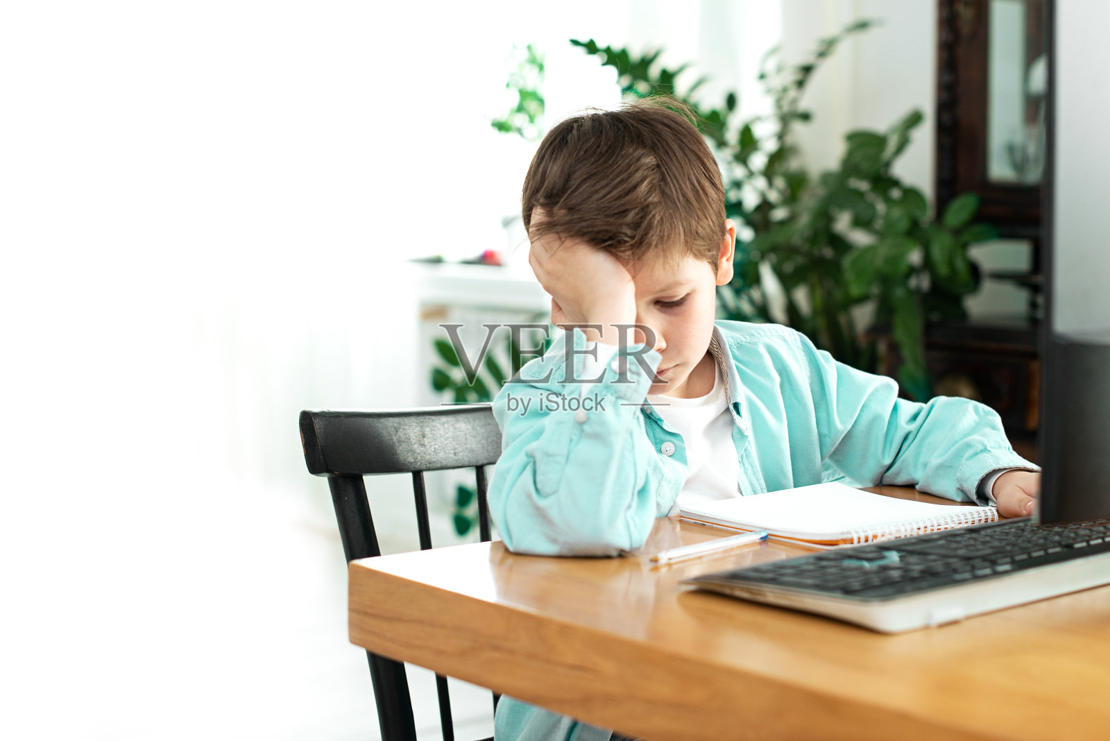 悲伤的孩子在写作业，沮丧的男学生在家进行远程学习，重返校园照片摄影图片