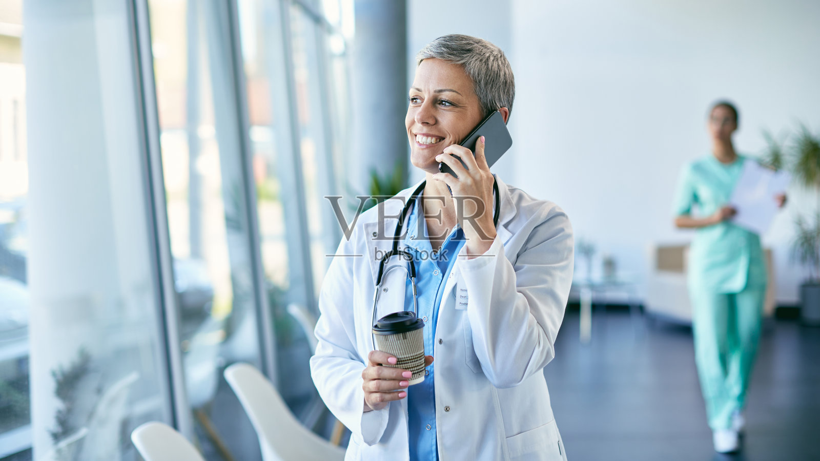 快乐的医疗工作者在她的医疗诊所的咖啡休息期间通过手机交流。照片摄影图片