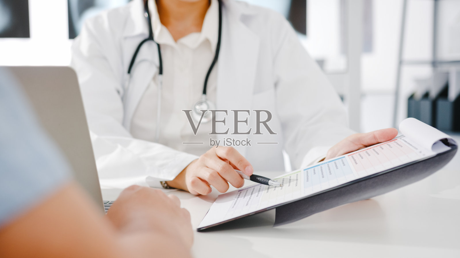 年轻的亚洲女医生正在用剪贴板传递好消息，谈论结果或症状与男性病人坐在健康诊所的桌子上。照片摄影图片