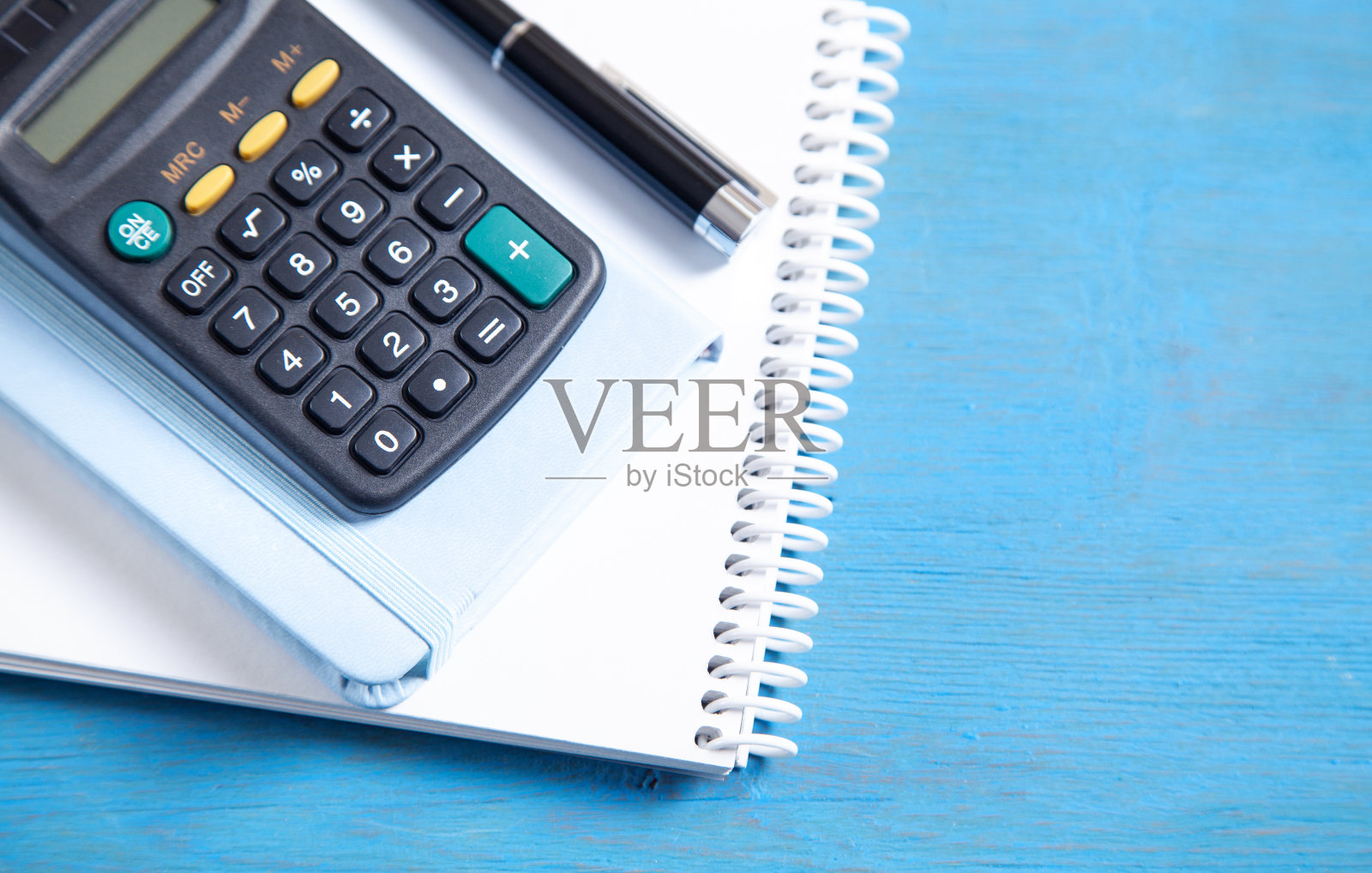 蓝色背景上的钢笔、记事本和计算器。照片摄影图片