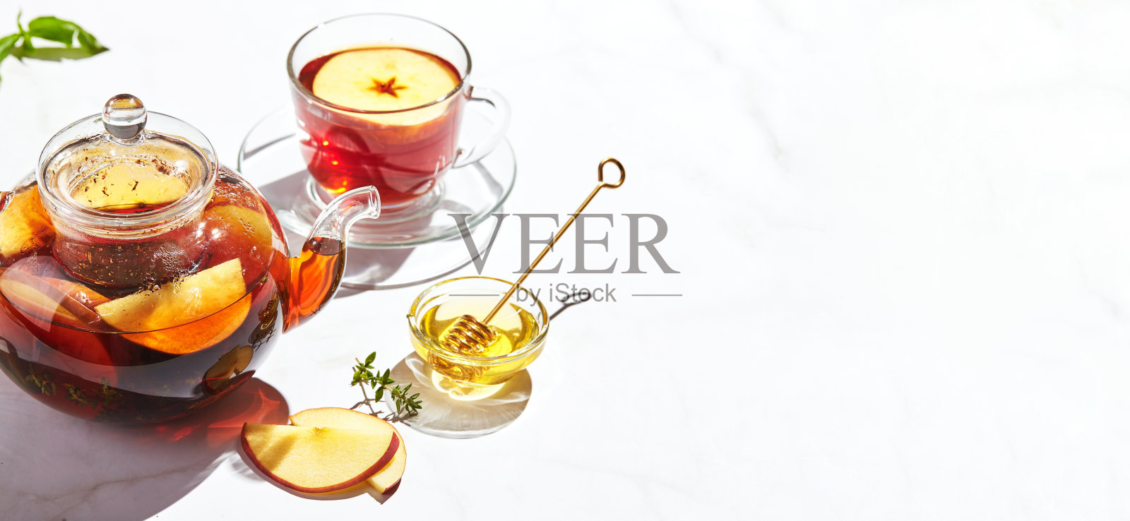 玻璃茶壶和杯子里的苹果、百里香和蜂蜜果茶，白色的背景上有坚硬的阴影照片摄影图片