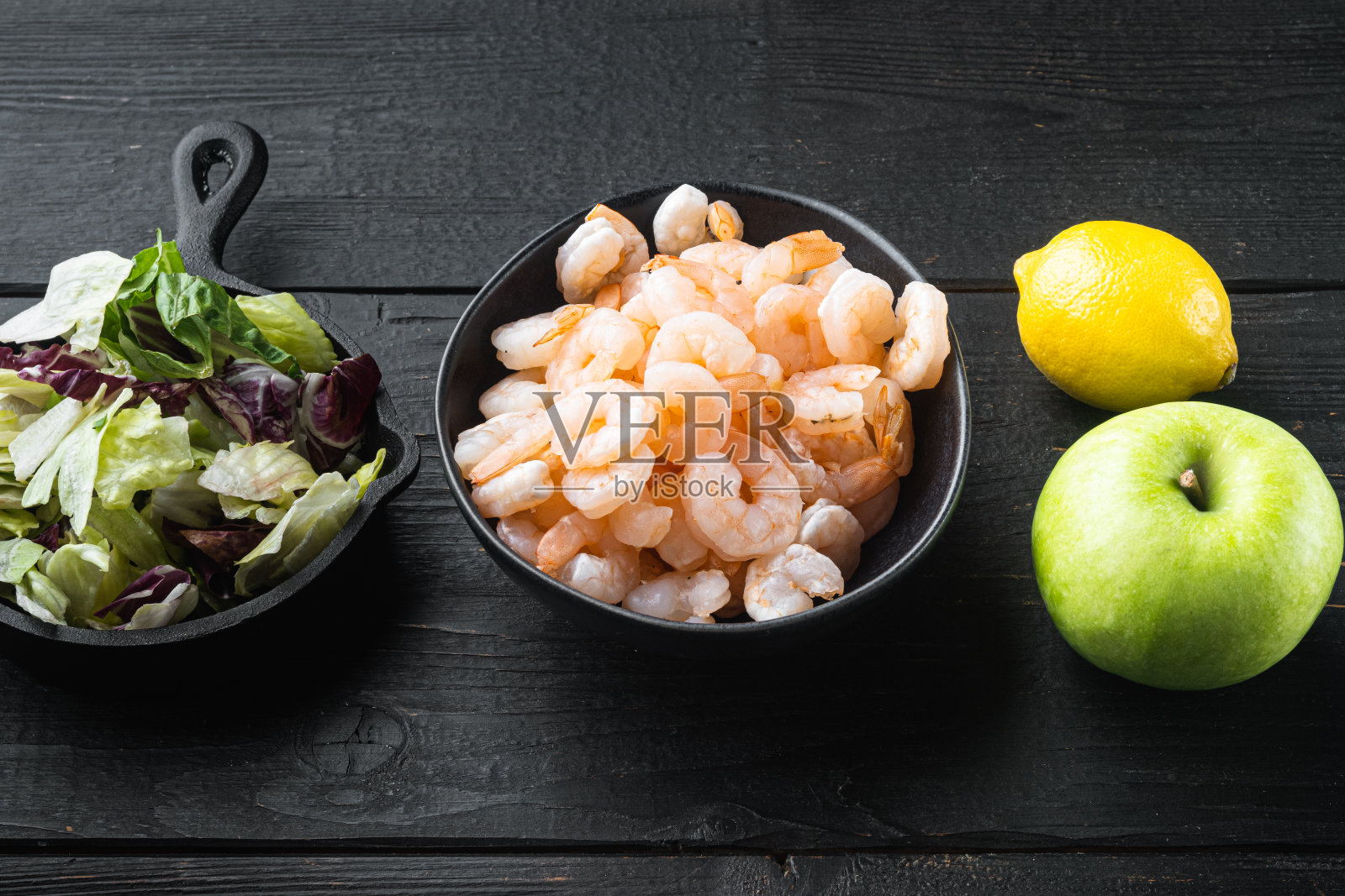 新鲜的夏季维他命开胃菜，绿叶沙拉，虾仁，橄榄配料，配酱苹果和葡萄，放在黑色木桌上照片摄影图片