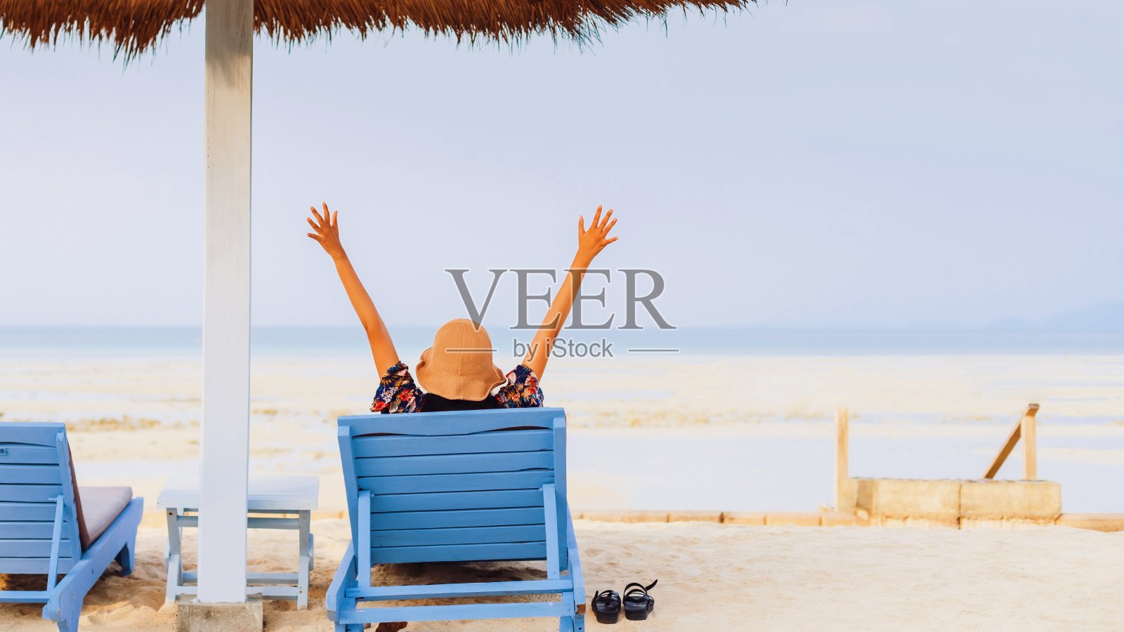 一名女游客懒洋洋地躺在海边的沙滩椅上，这是一个夏日，背景是蓝天。周末快乐旅行的概念。照片摄影图片