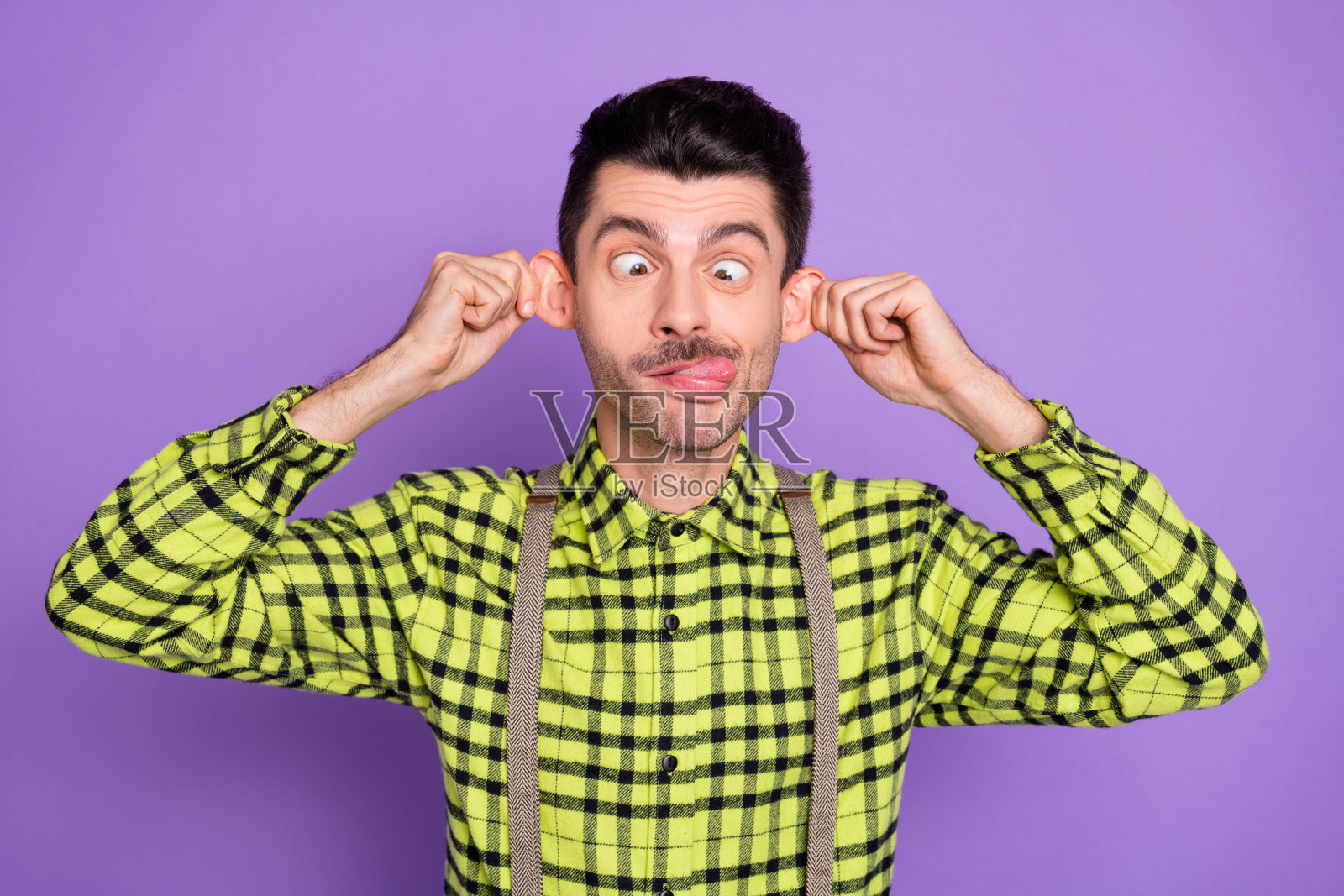 年轻的funky滑稽幽默的傻孩子的照片男人伸出舌头拉耳朵孤立在紫色的背景照片摄影图片