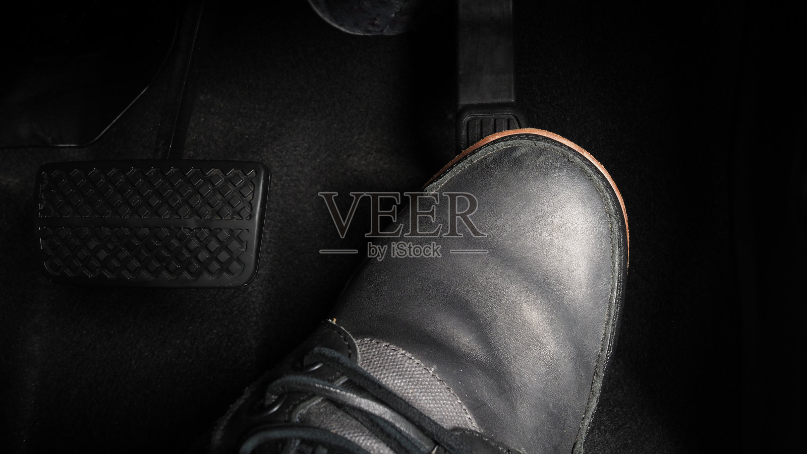 在开车时踩汽车的脚踏板。汽车的油门和刹车踏板。司机驾驶汽车通过推动加速器和刹车踏板的汽车。车辆内部。控制踏板。关闭了。照片摄影图片