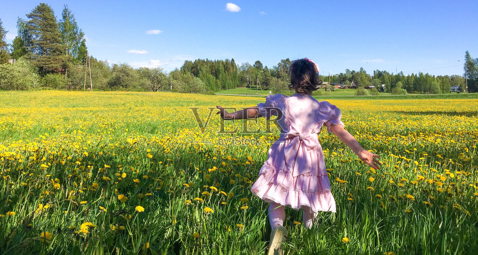 一个白人女孩跑过一片长满黄色蒲公英的空地。孩子在温暖的夏天快乐，照片摄影图片
