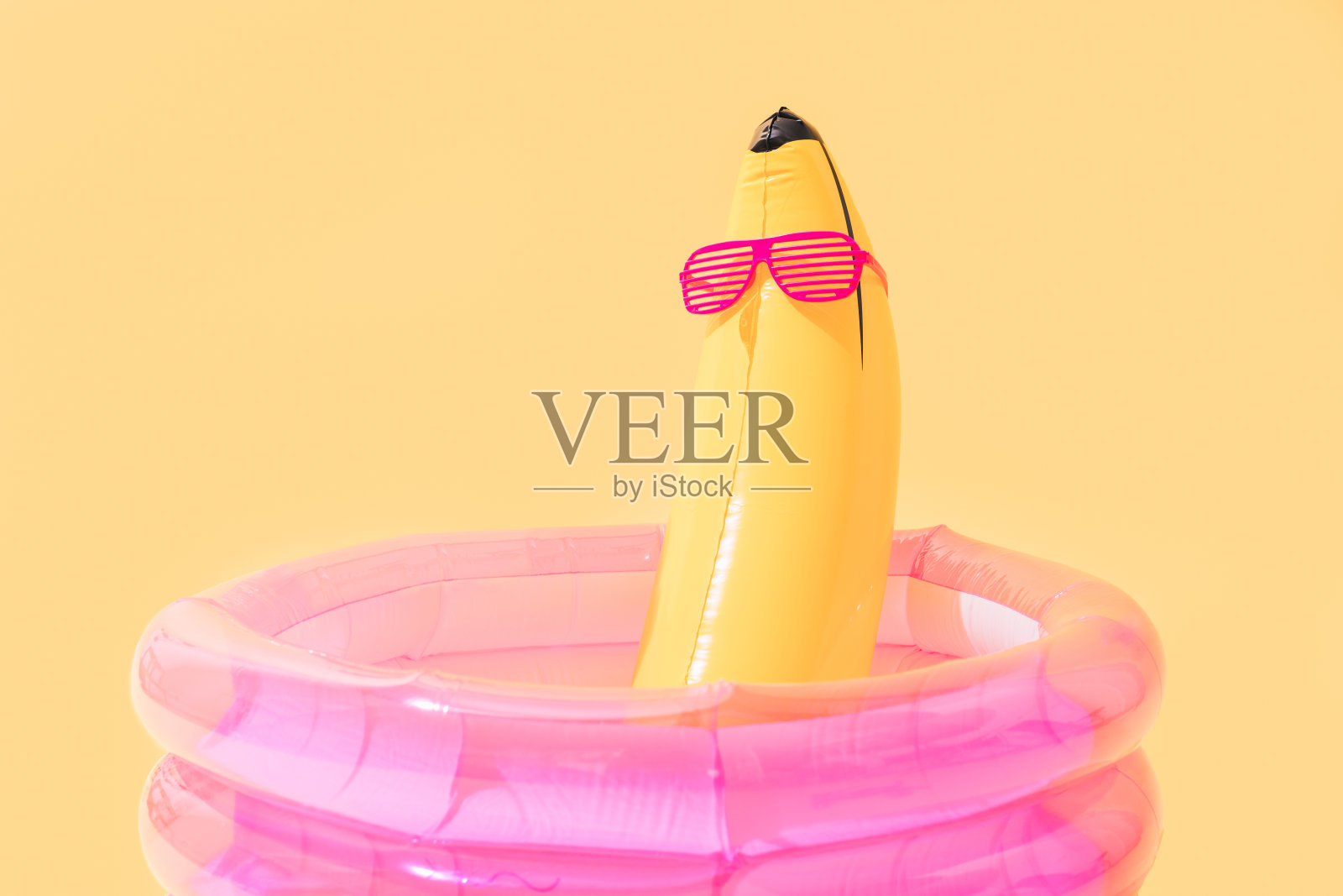 儿童游泳池，香蕉形状的充气香蕉，黄色背景上有太阳镜。照片摄影图片