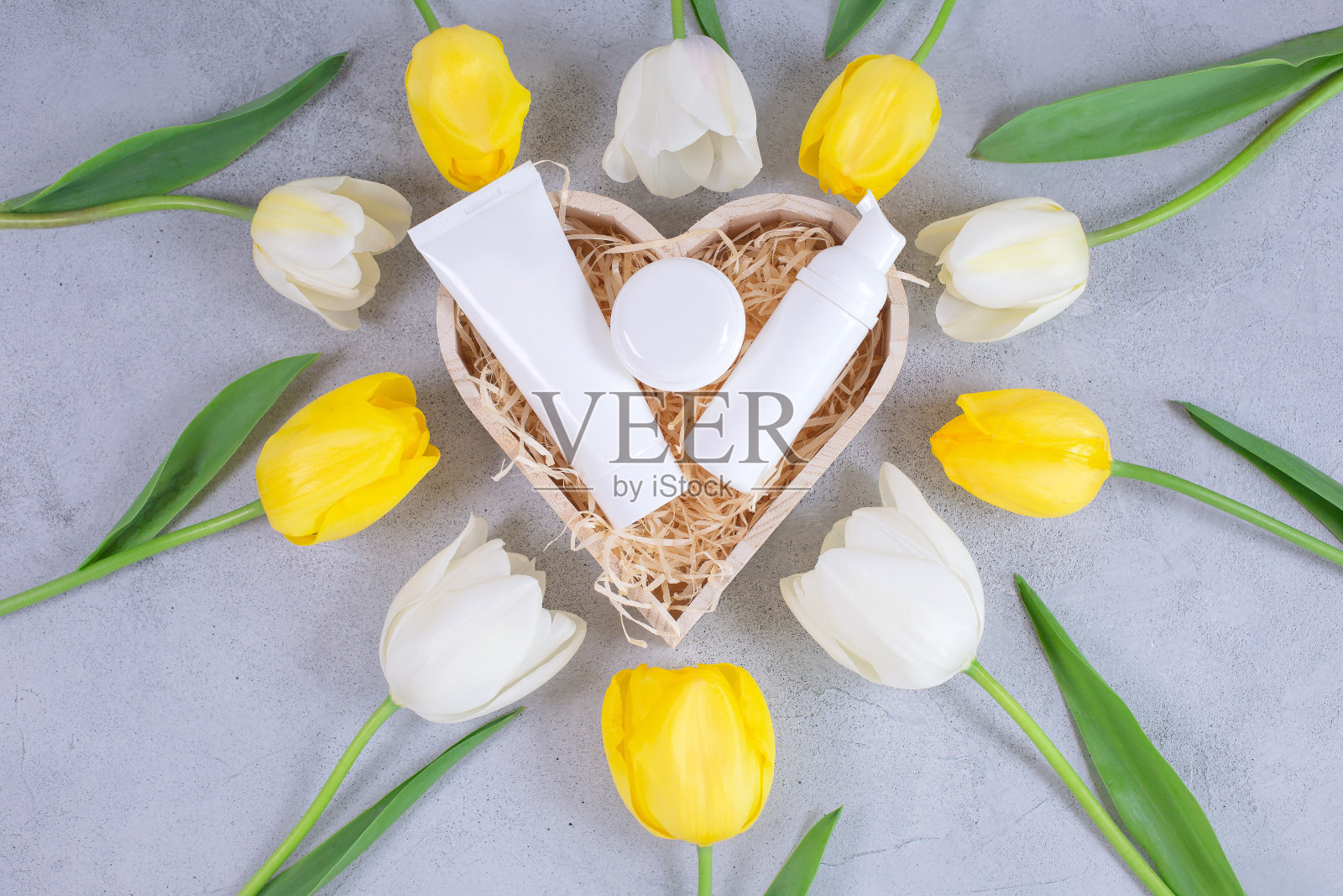 白色的化妆品瓶子和容器上的礼物木盒周围的郁金香花。照片摄影图片