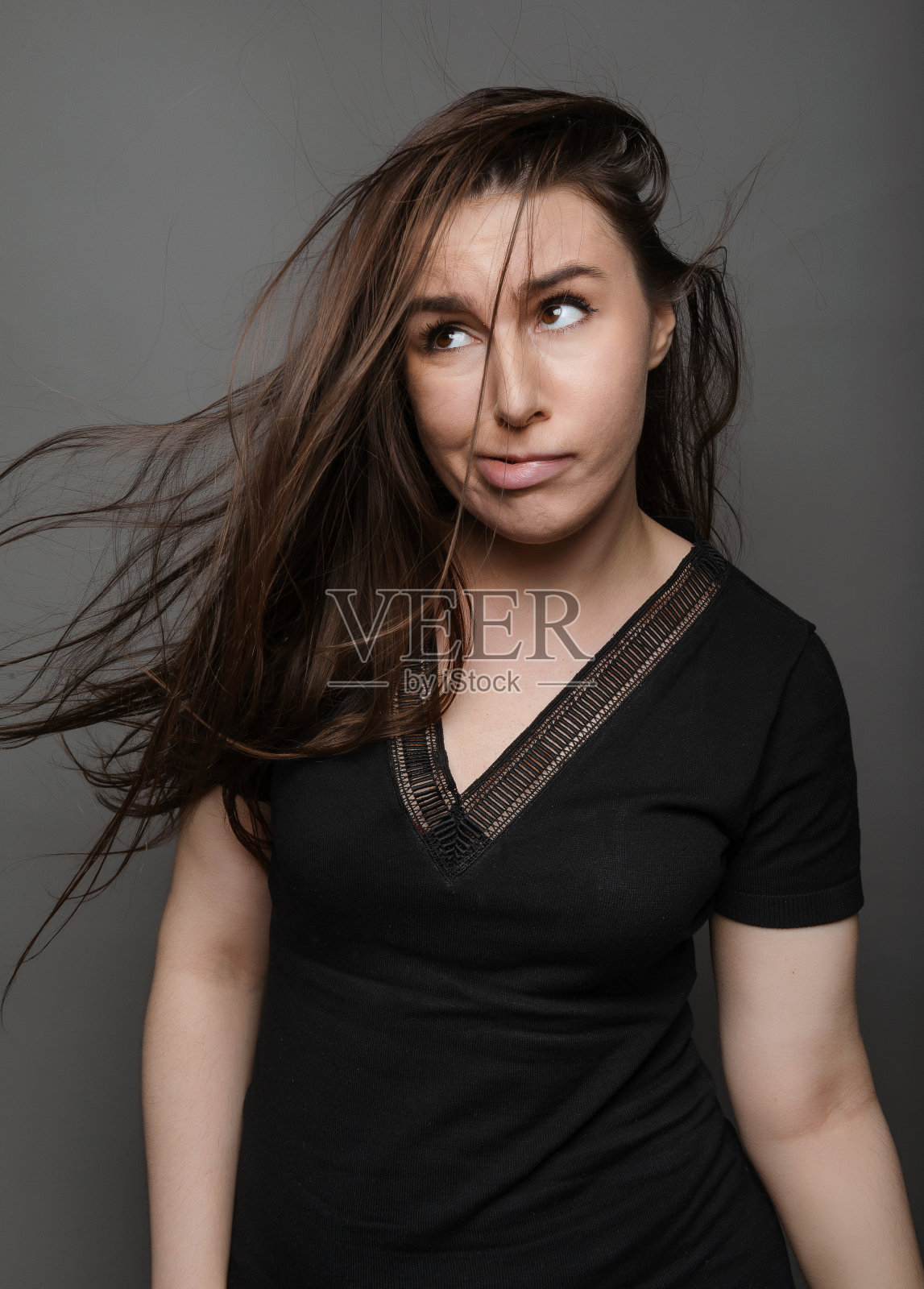 有趣的年轻女子，长头发，黑色上衣，灰色背景照片摄影图片
