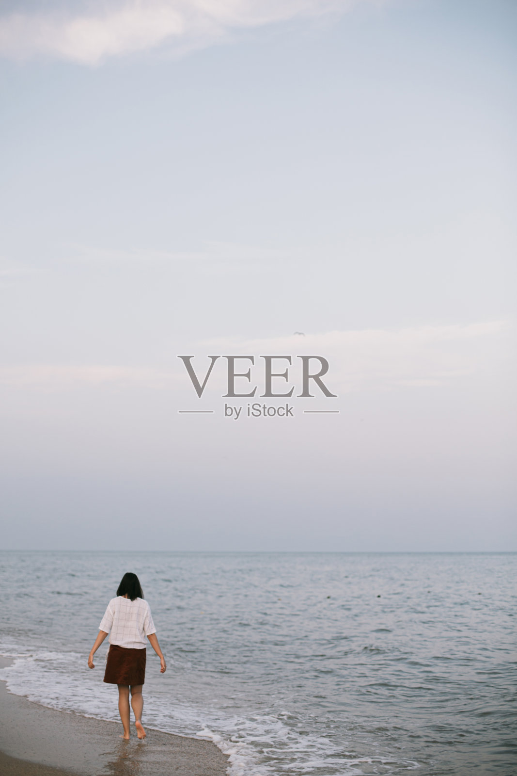 无忧无虑的潮女人赤脚走在冰冷的海浪沙滩上，享受宁静的夜晚照片摄影图片