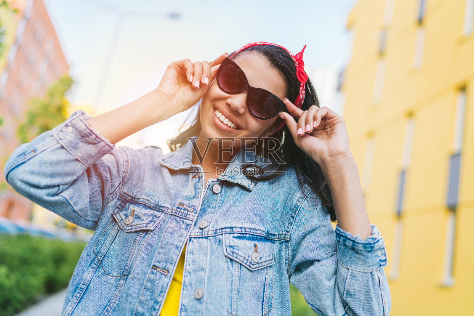 美丽的快乐微笑的非洲裔美国嬉皮士女孩的肖像在户外摆出时尚的太阳镜和牛仔夹克与红色的头巾蝴蝶结在她的头上照片摄影图片