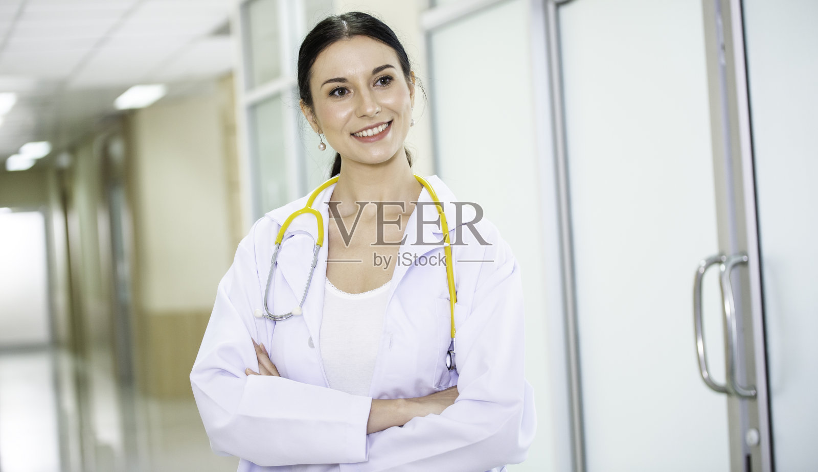 肖像快乐的白人女医生与听诊器微笑在双臂交叉看着相机。一个女人站在医院走廊上医疗卫生服务。本空间照片摄影图片