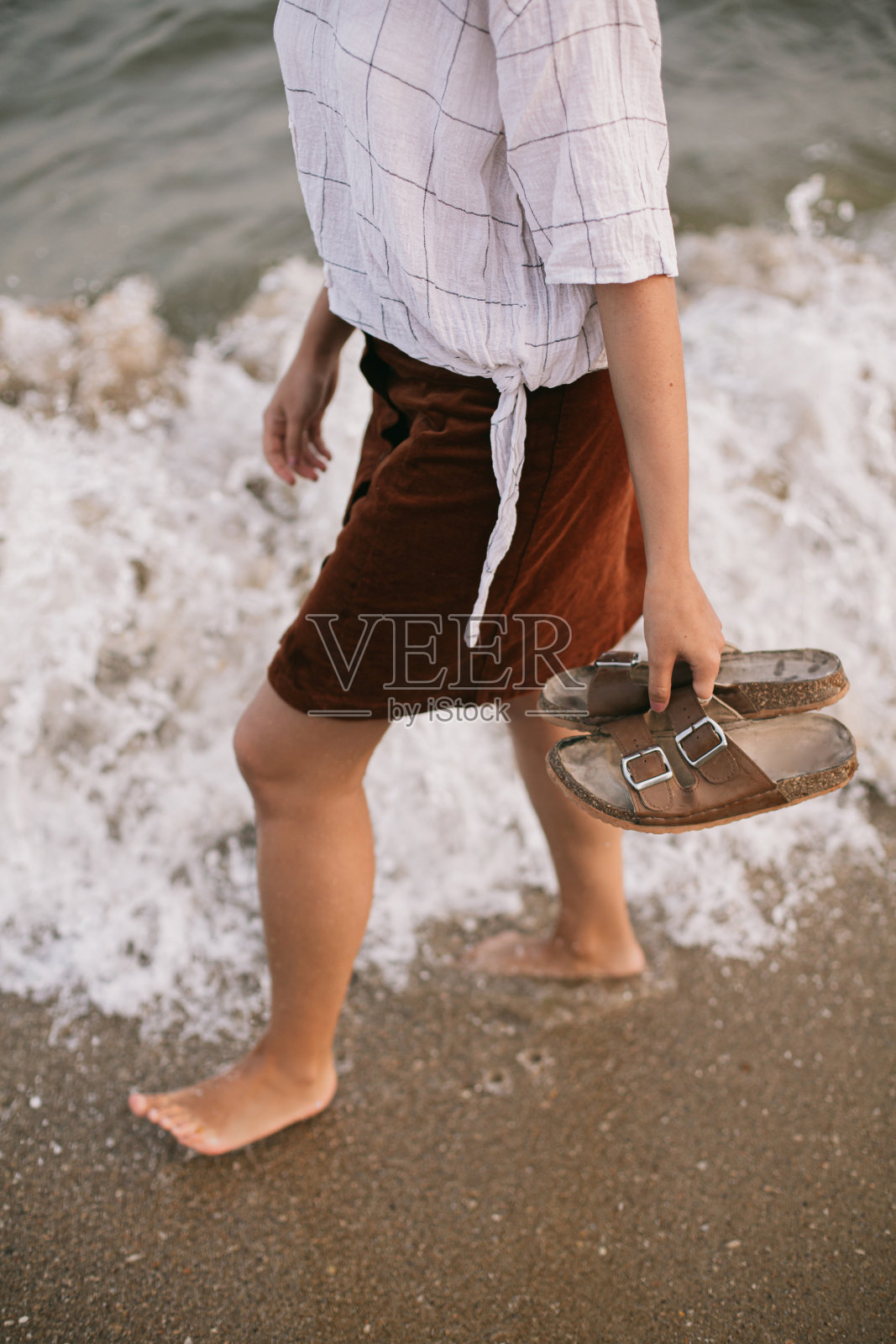 无忧无虑的时髦女人赤脚走在海滩上的海浪，手拿拖鞋。正念照片摄影图片