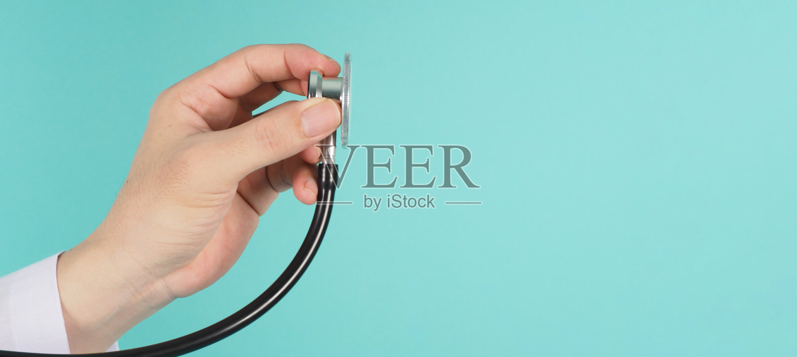 医生手持听诊器的特写，身着薄荷绿或蒂芙尼蓝背景的长袖长袍。照片摄影图片