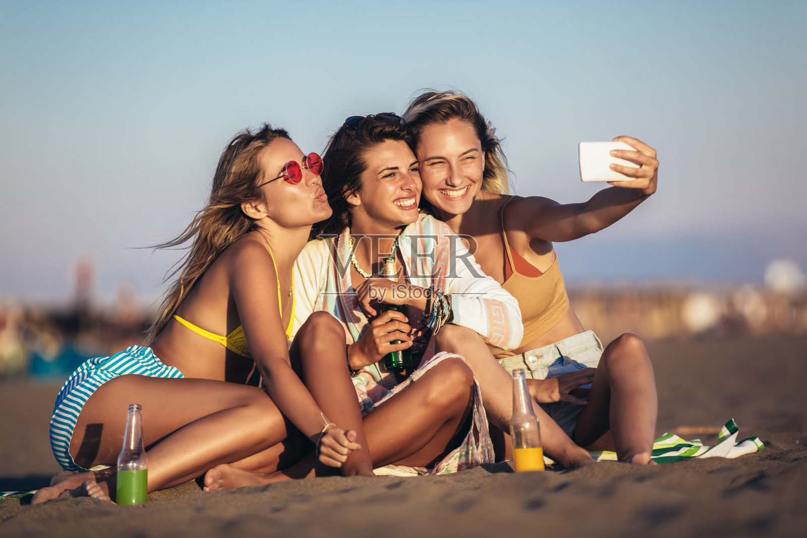 坐在海滩上快乐的年轻女人。一群享受海滩度假的朋友。照片摄影图片