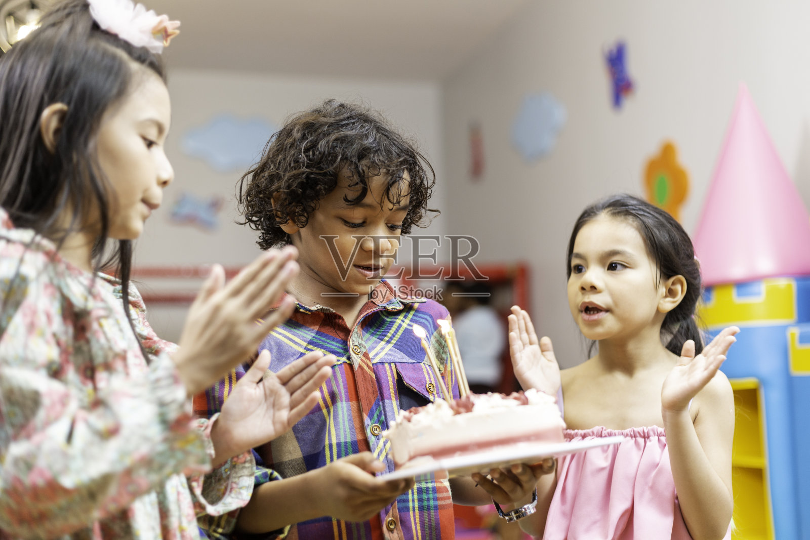 小男孩在生日聚会上吹蛋糕，和朋友们一起在游戏室鼓掌。照片摄影图片