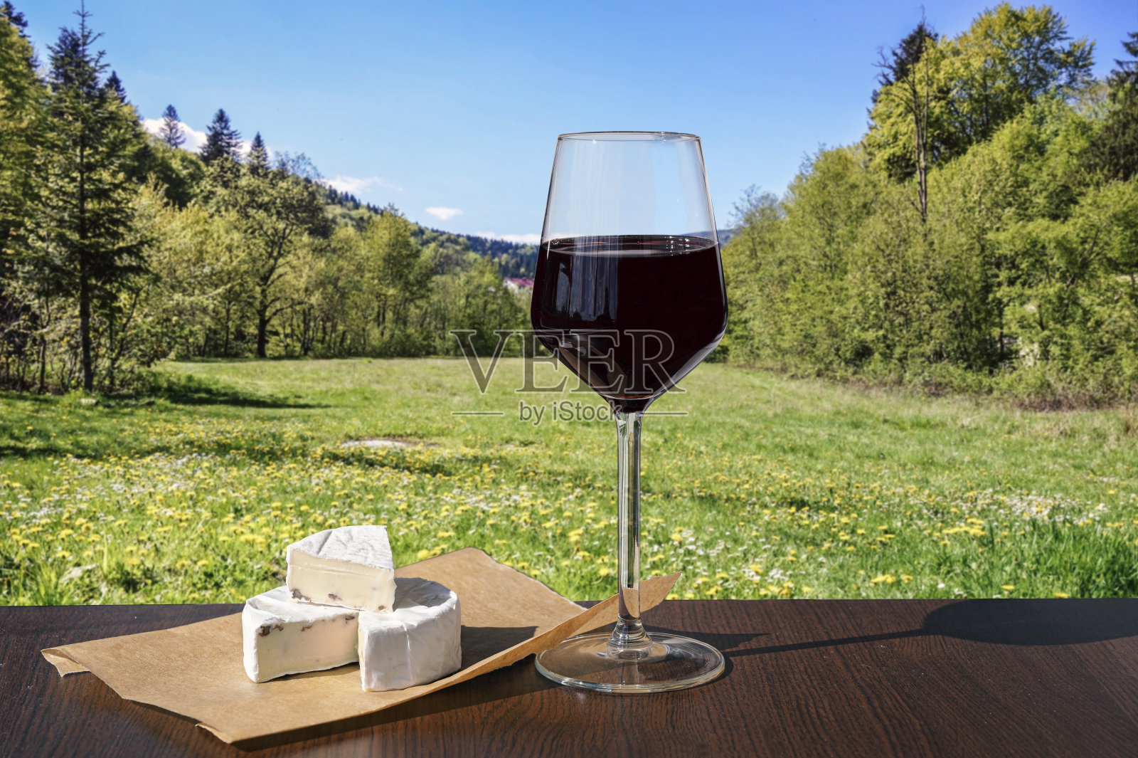 一杯红酒和布里干酪，映衬着绿油油的草地和黄白相间的花朵照片摄影图片