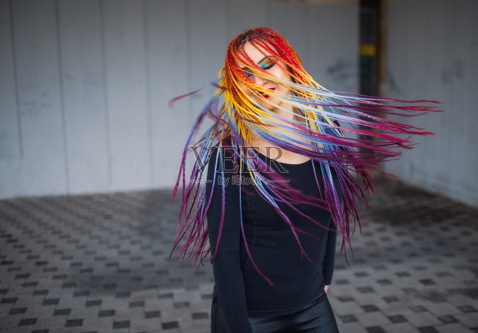 一个不寻常的优雅的女孩穿着黑色的简单的衣服，明亮的化妆和多色的辫子在一个旧建筑的背景下摆姿势照片摄影图片