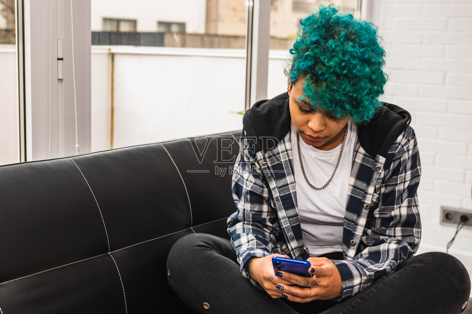 在家里或公寓里有手机的蓝色头发的美国黑人卷发的年轻女子或女孩照片摄影图片