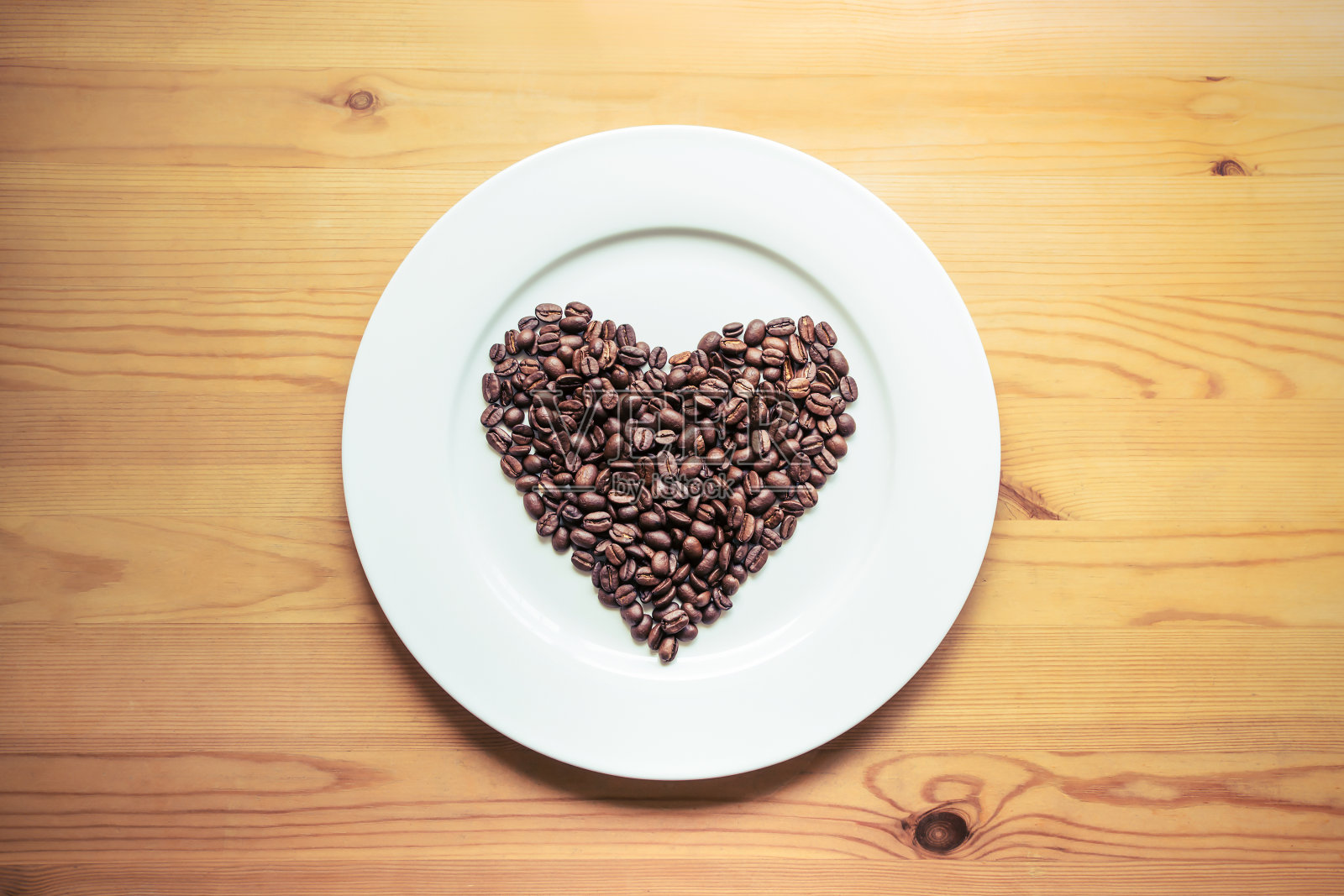 用咖啡豆制成的心放在木桌上的白色盘子上，俯视图照片摄影图片