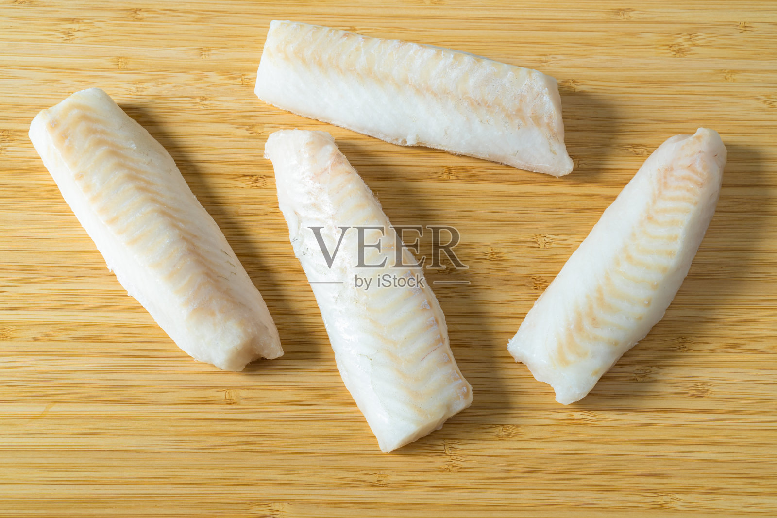 生的冷冻鳕鱼片或腰肉放在木砧板上。照片摄影图片