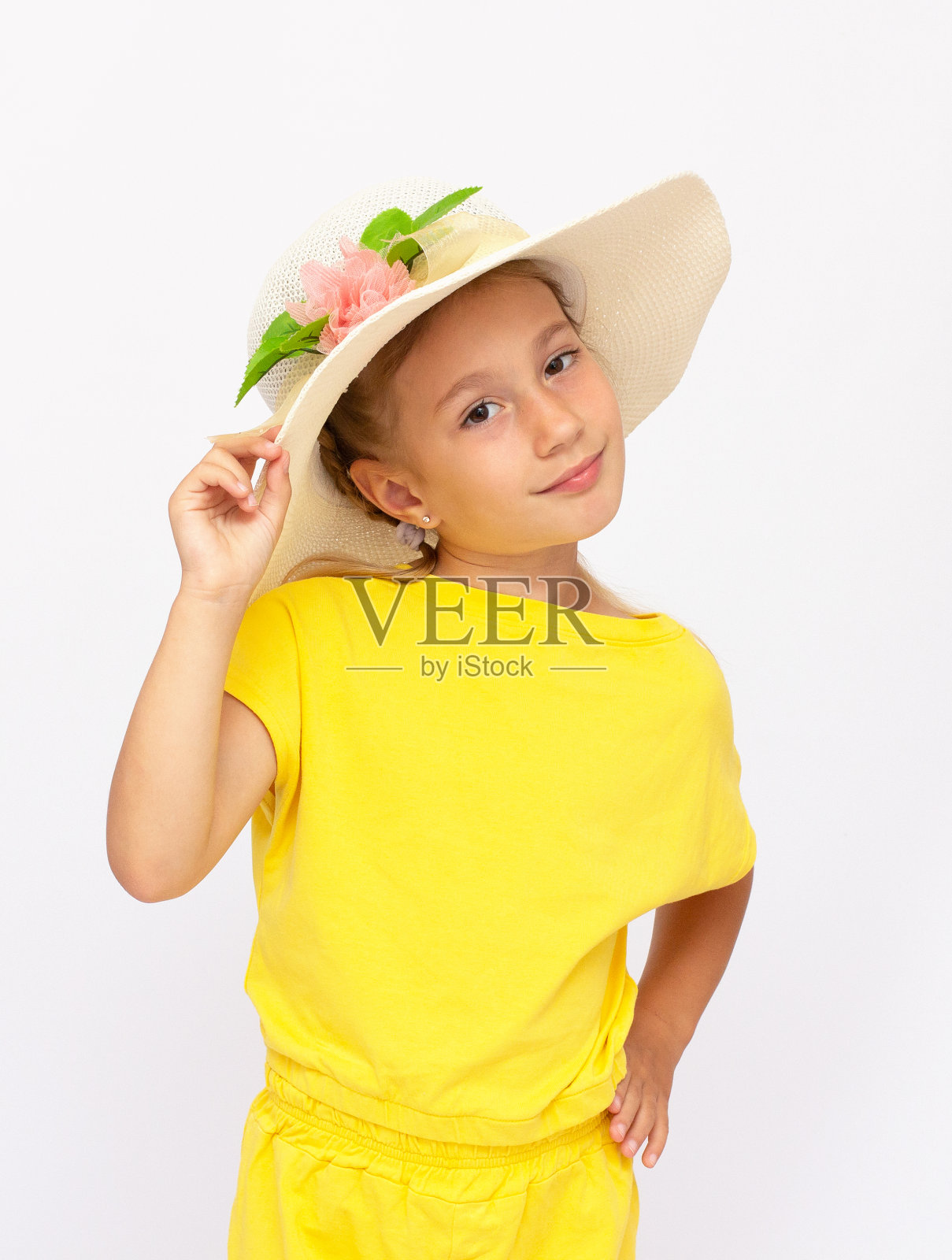 平静的小女孩站在黄色t恤和巴拿马草帽，孤立在白色的背景照片摄影图片